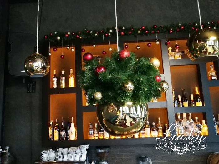 Подвесной шарообразный светильник над баром с новогодним украшением на фоне стеллажа